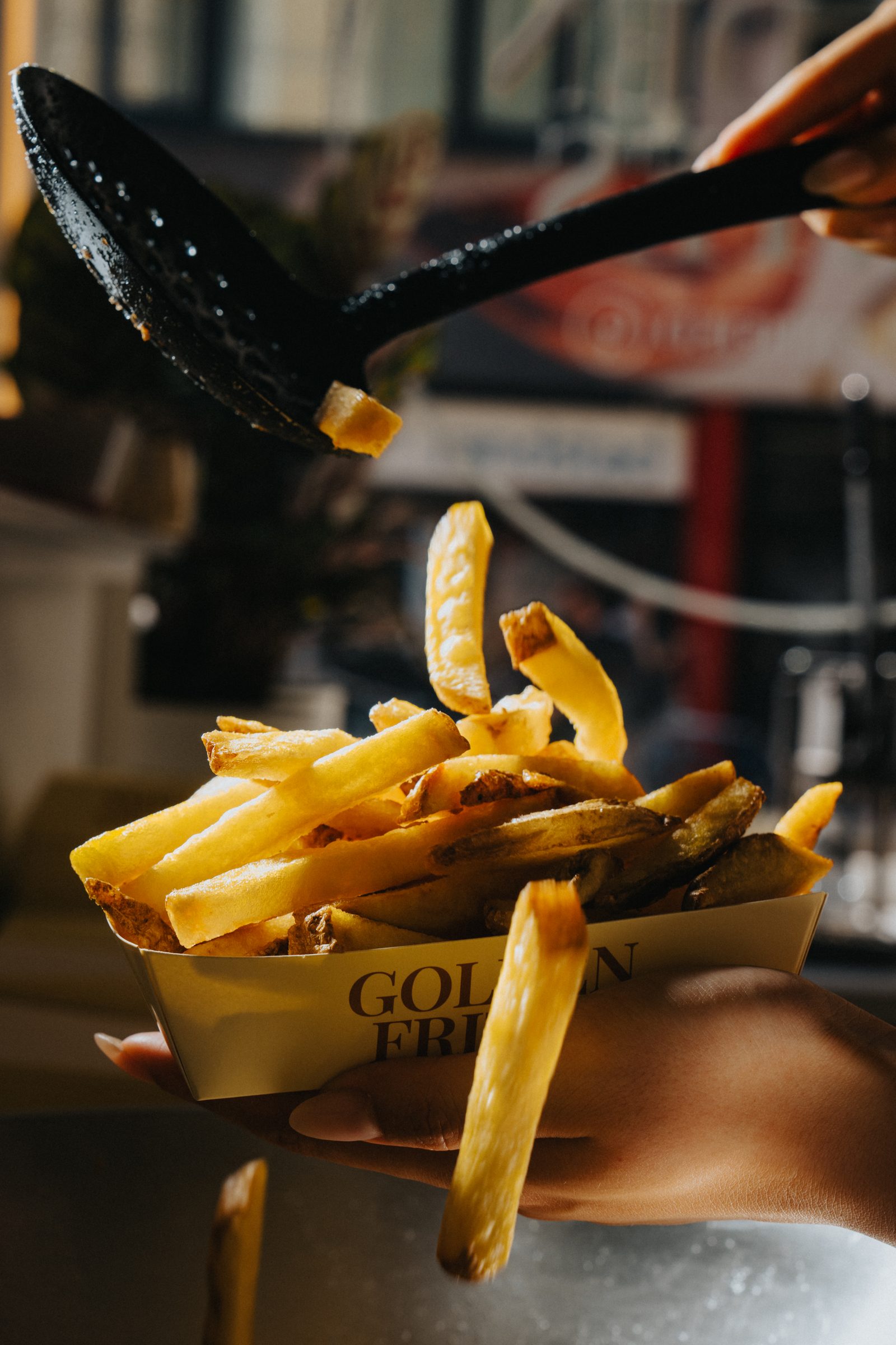A paper cone of golden frites on a warm cream background